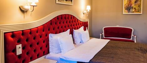A hotel room with a red tufted headboard, white bedding, a bedside table, and two wall-mounted lamps.