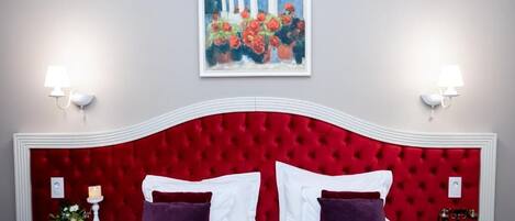 A hotel room with a red upholstered headboard, white bedding, and two bedside tables with lamps.