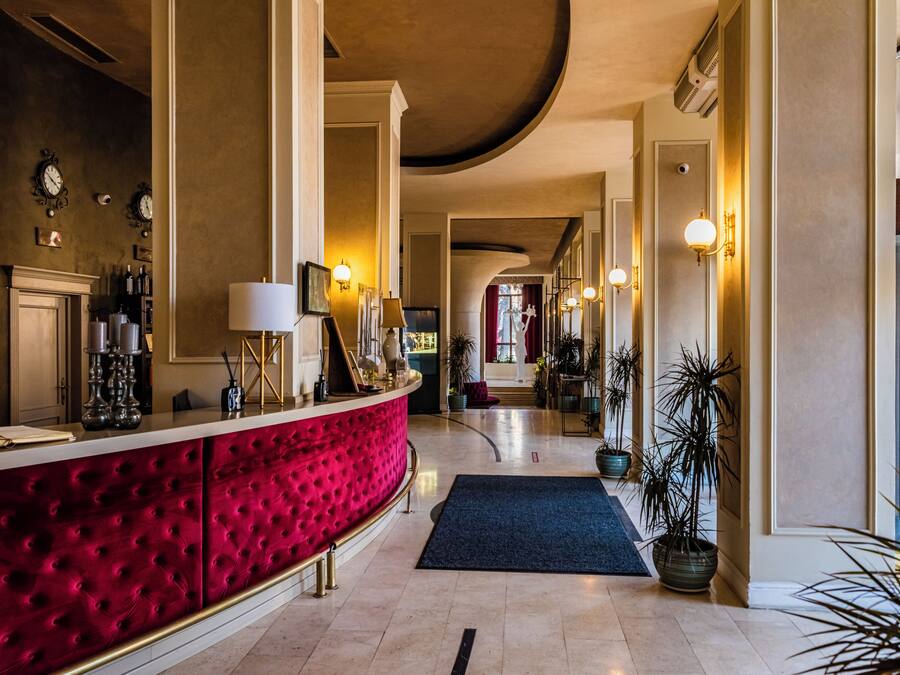 En hotellobby med en röd sammetsbeklädd receptionsdisk, ett marmorgolv och utsikt över gatan genom stora fönster.