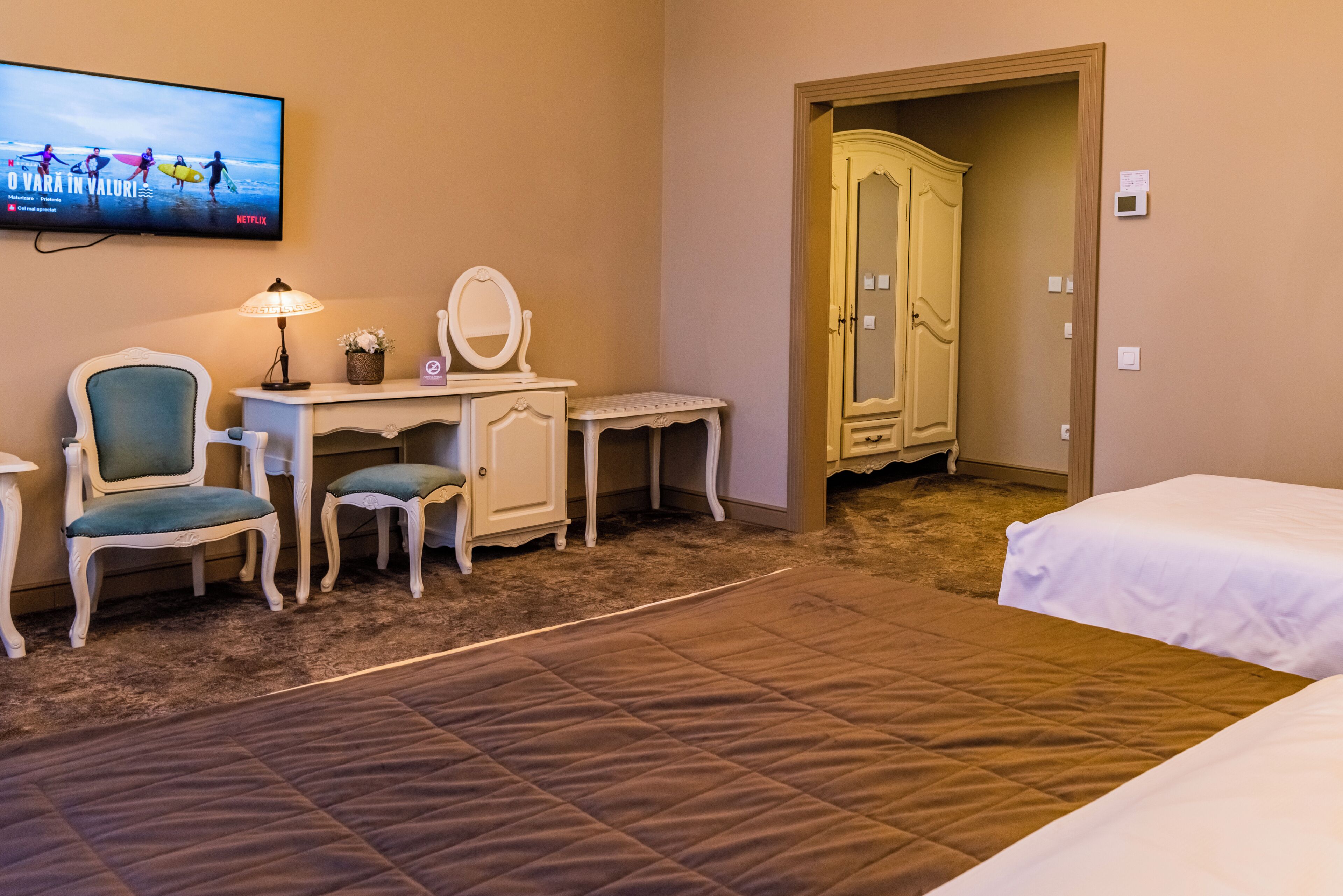 A hotel room with a bed, a desk with a chair, a vanity with a mirror, and a wardrobe.
