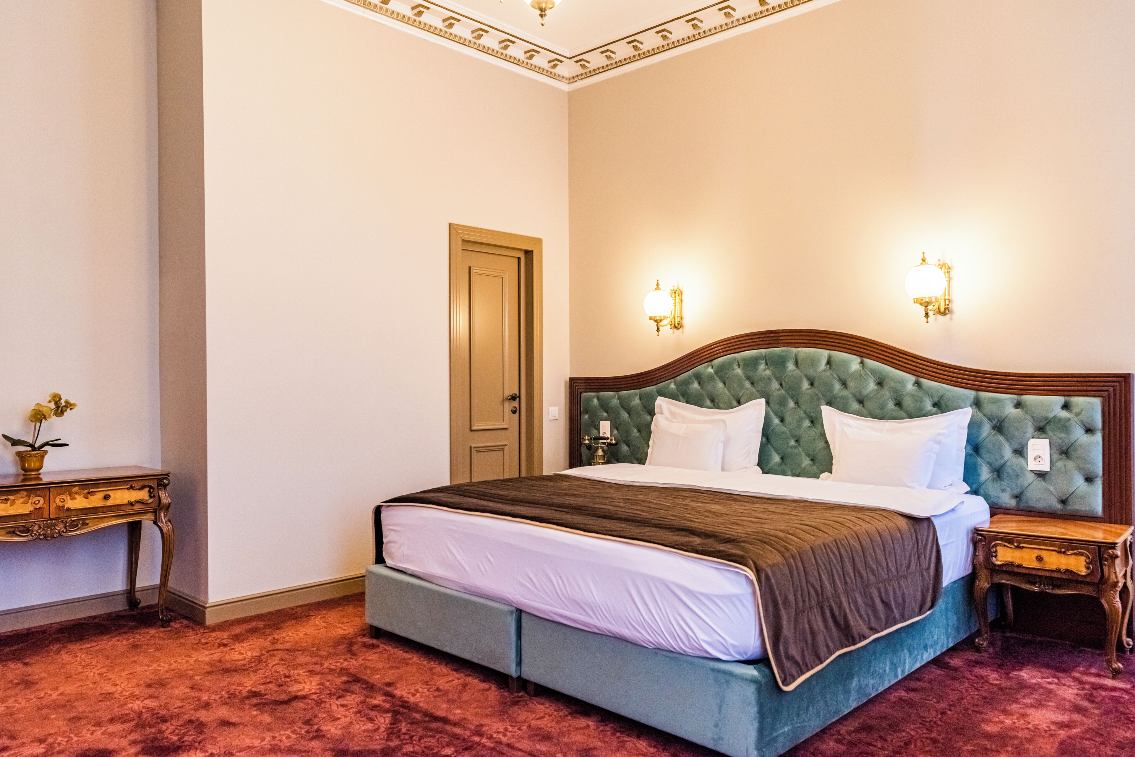 Une chambre d’hôtel avec un grand lit, une table de chevet en bois, une petite table avec un vase et une porte.
