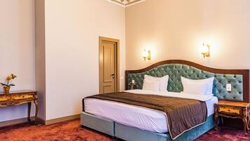 A hotel room with a large bed, a wooden nightstand, a small table with a vase, and a door.