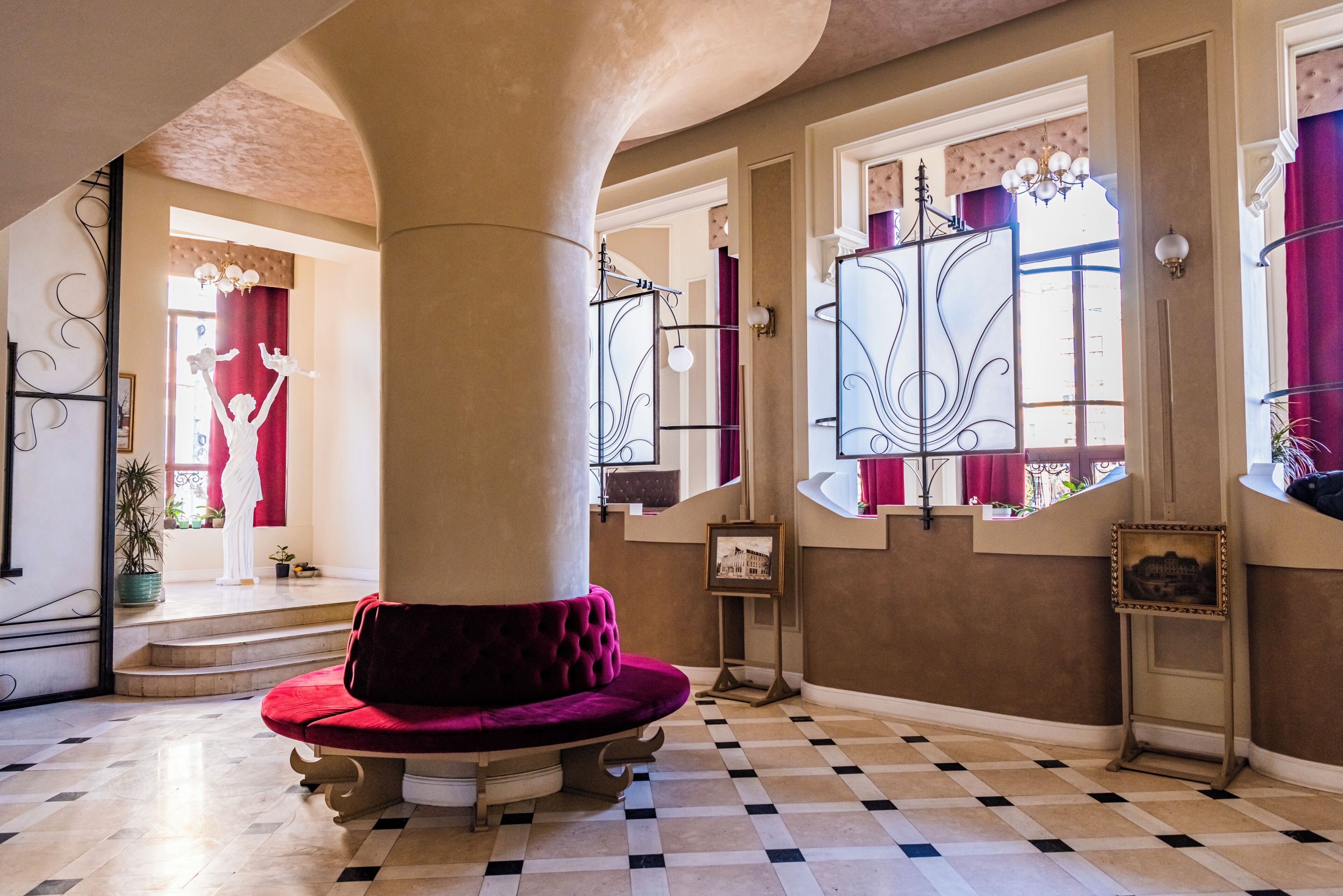 A spacious interior with a checkered floor, a large column, and a red velvet bench.