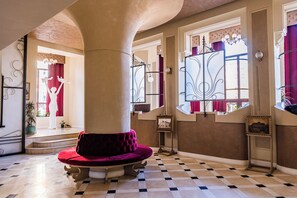 A spacious interior with a checkered floor, a large column, and a red velvet bench. - Grand Hotel Traian (Iași)