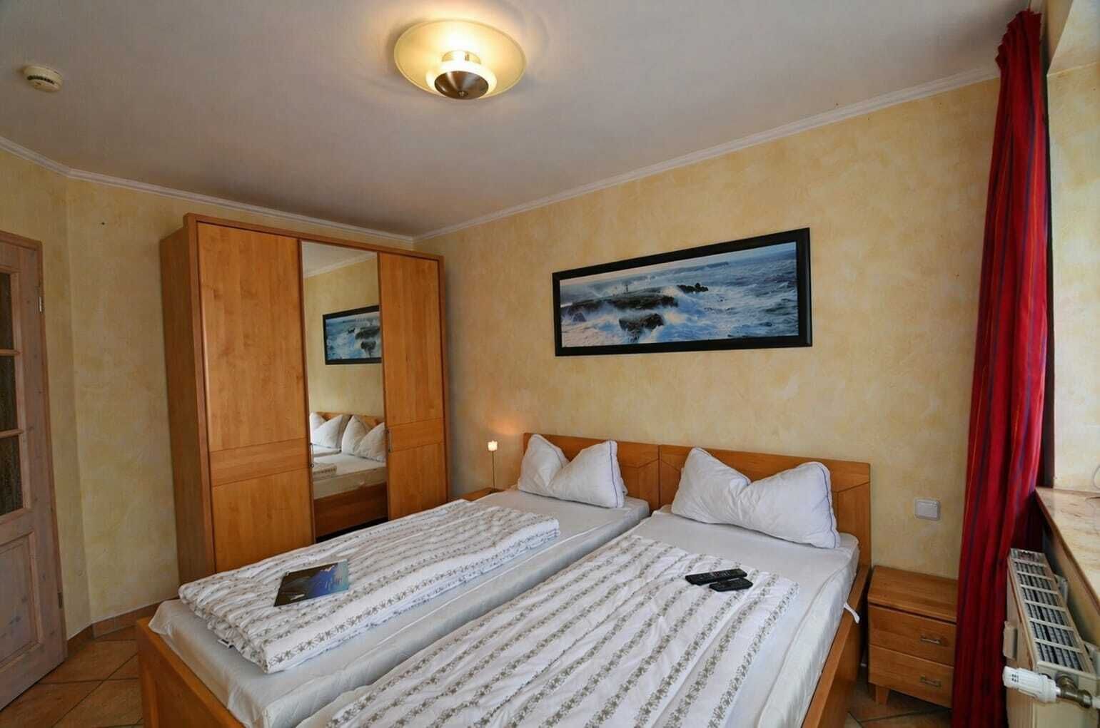 A double bed with a headboard, a bedside table, a nightstand, a mirror, a painting, and a red curtain.