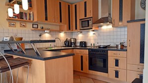 A modern kitchen with wooden cabinets, a central island, a microwave, a stove, and bar stools. - About 50 meters to the sandy beach and the boardwalk, Wi-Fi, washing machine, about 300 meters to the harbor (Glowe)