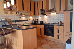 Eine moderne Küche mit Holzschränken, einer Kochinsel, einer Mikrowelle, einem Herd und Barhocker.