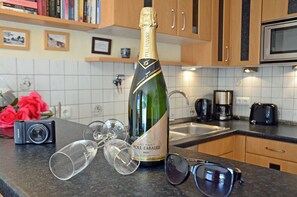 Eine Champagnerflasche, Gläser, eine Kamera und eine Sonnenbrille auf einer Küchenarbeitsplatte.