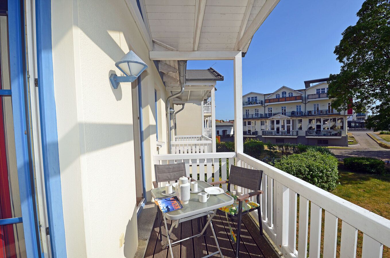 A balcony with a table and chairs, a white railing, and a view of residential buildings.