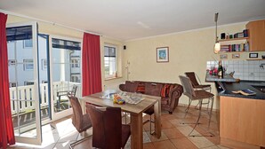 A dining area with a table and chairs, a kitchen with a counter, and a view of a building through a glass door. - About 50 meters to the sandy beach and the boardwalk, Wi-Fi, washing machine, about 300 meters to the harbor (Glowe)