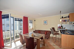 A dining area with a table and chairs, a kitchen with a counter, and a view of a building through a glass door.