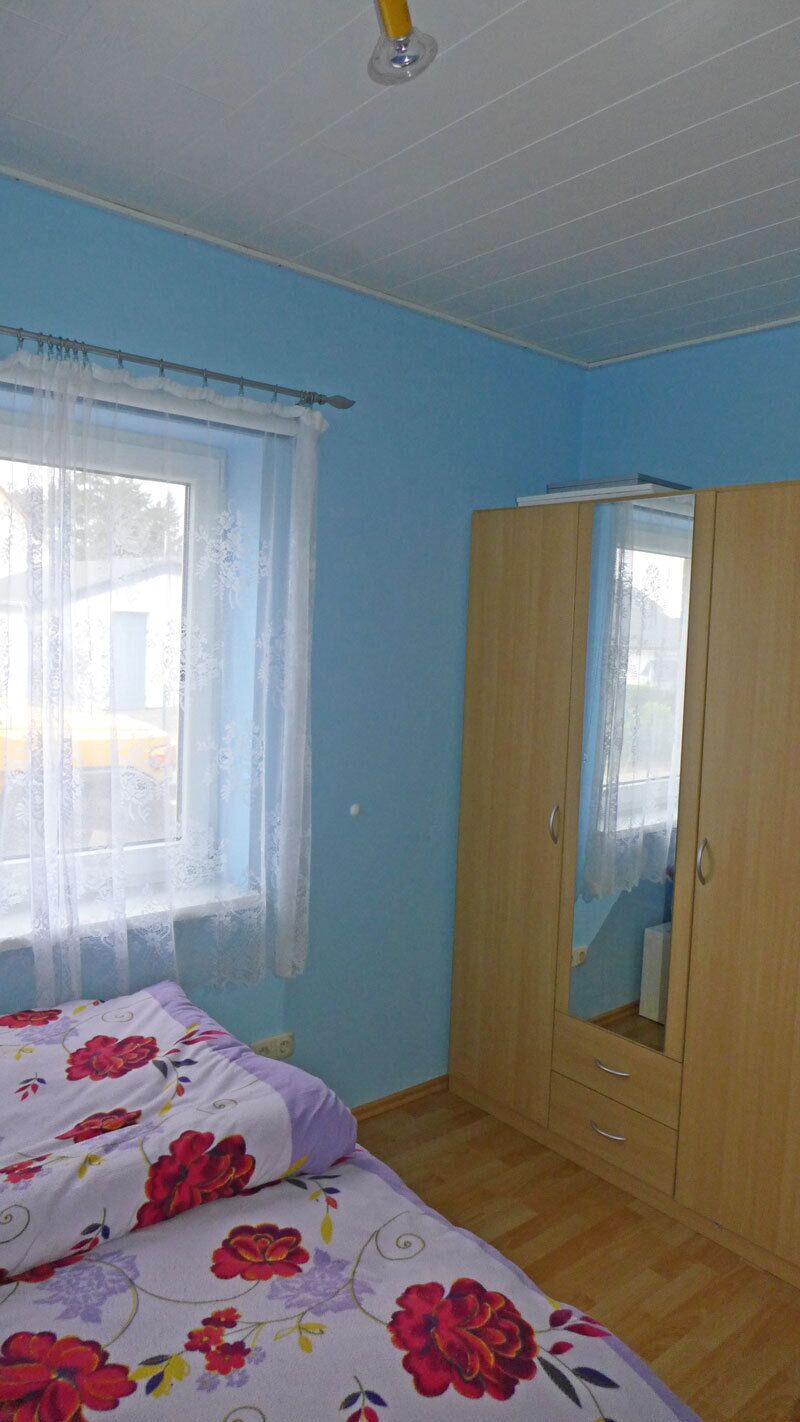 Un dormitorio con cama, armario y ventana con cortinas.
