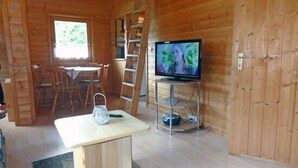 Interior de madeira com mesa de jantar, cadeiras, televisão em um móvel e uma escada.