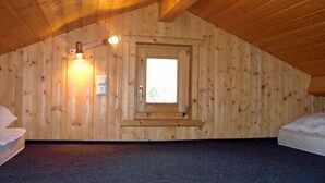 Um quarto com teto inclinado, uma janela com porta e piso coberto de carpete.