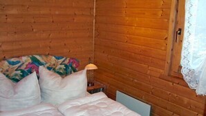 Quarto de cabana de madeira com cama, almofadas, mesa de cabeceira e abajur.