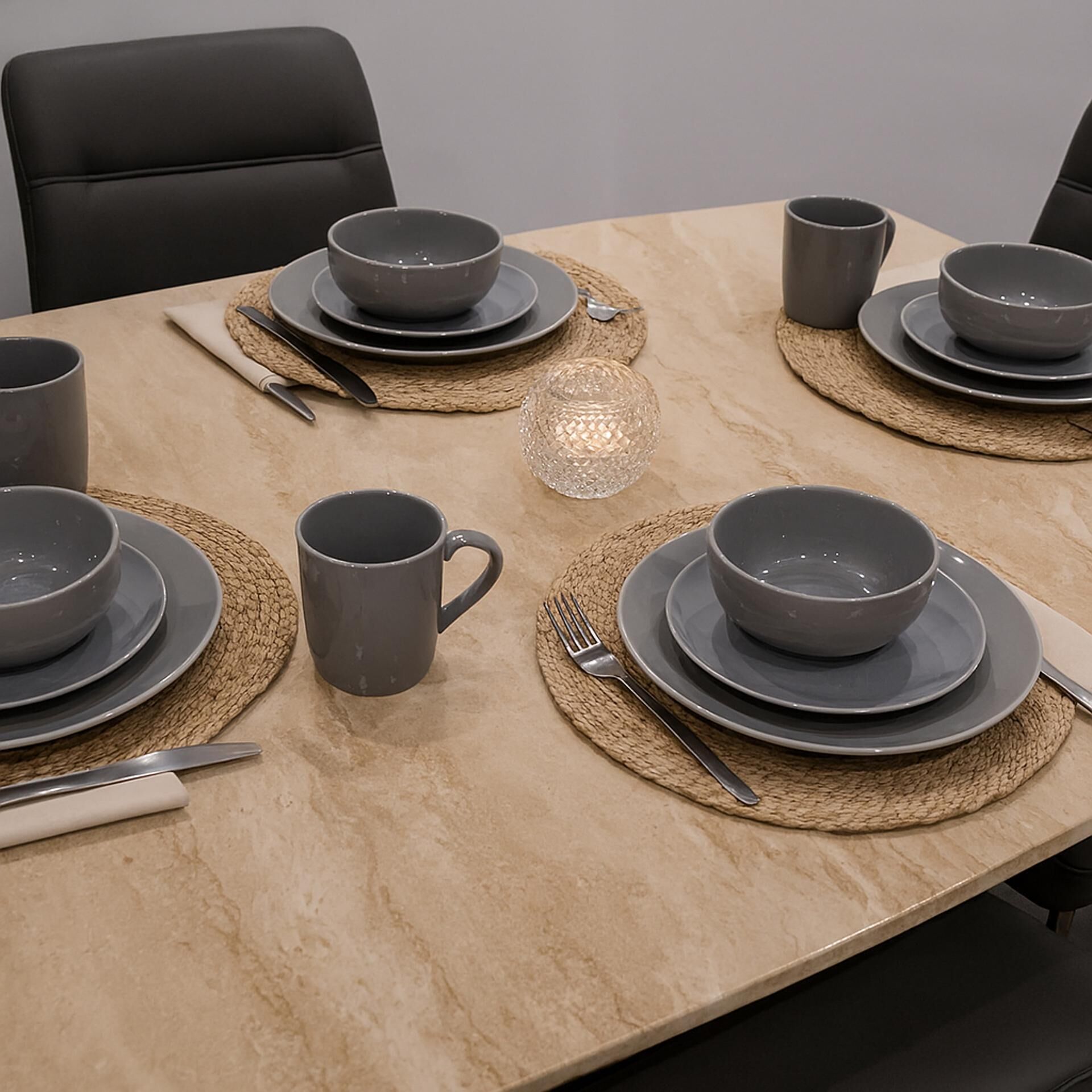 A table set with grey bowls, cups, and cutlery on woven placemats.