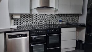Cozinha moderna com eletrodomésticos de aço inoxidável, bancada preta e painel de azulejos.