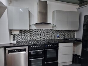 A modern kitchen with stainless steel appliances, a black countertop, and a tiled backsplash. - Modern 3BD House W/smarttv & Free Parking! (Romford)
