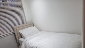Uma cama de solteiro com cabeceira, roupa de cama branca e janela com persianas.