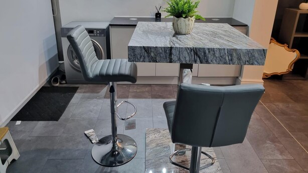 Uma cozinha moderna com bancada de mármore, máquina de lavar embutida e área de refeições com cadeirinha e mesa pequena.