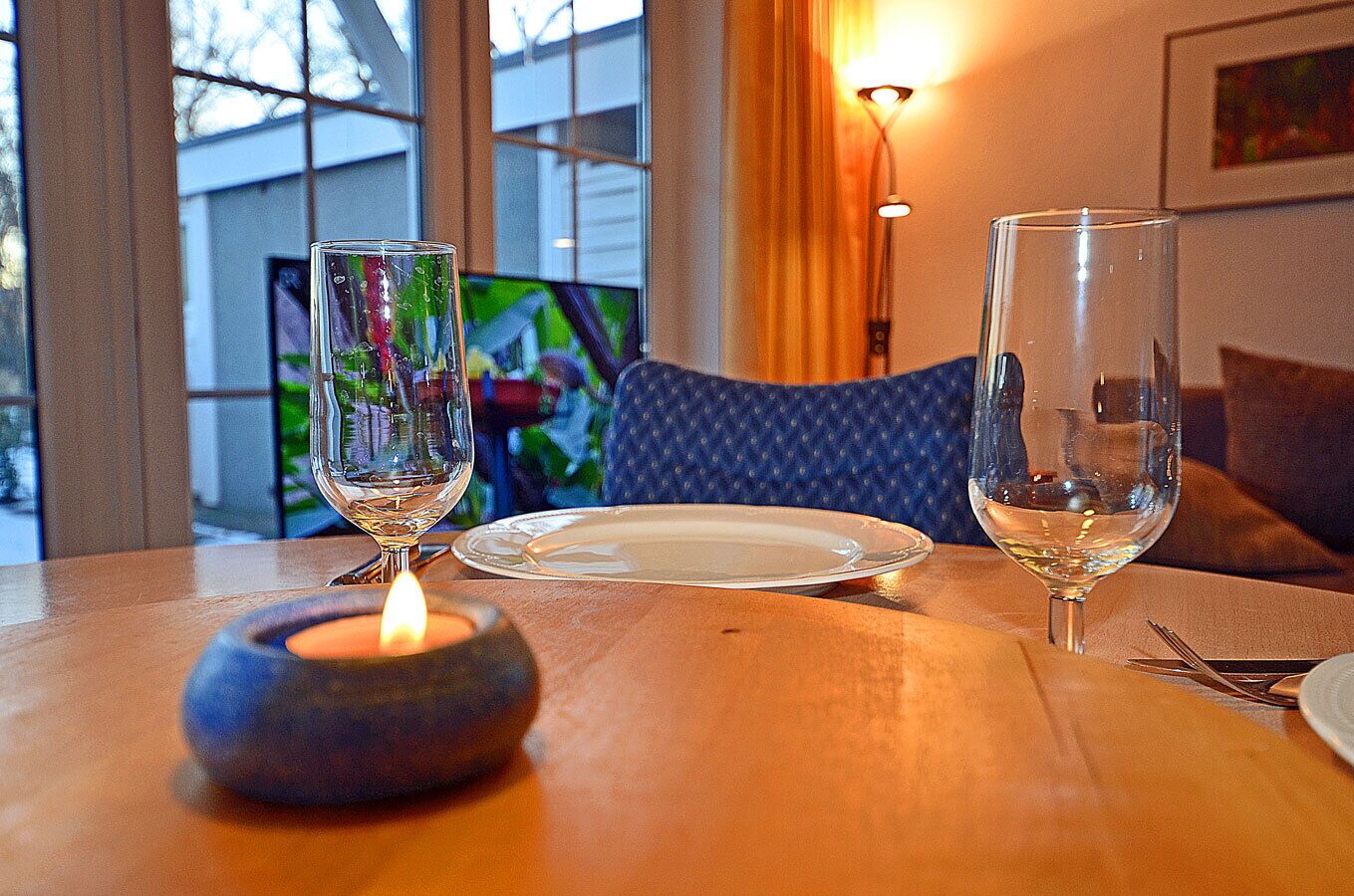 A dining table with two wine glasses, a candle, and a plate.