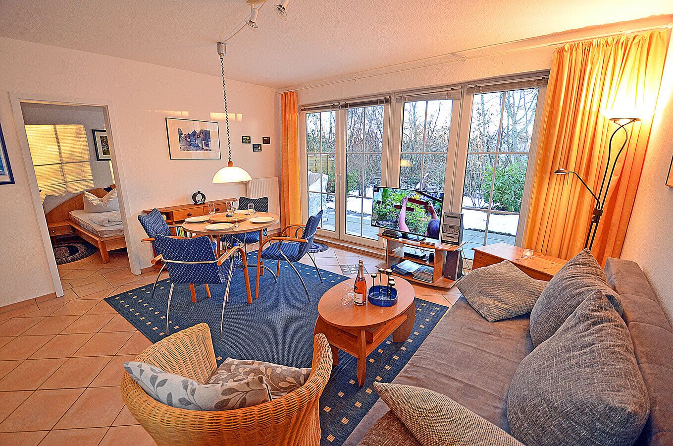 A living room with a sofa, a dining table, chairs, a TV, and a window with curtains.
