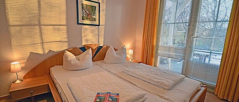 Een hotelkamer met een bed, bedlampjes, een lijst aan de muur en een raam met zonwering.