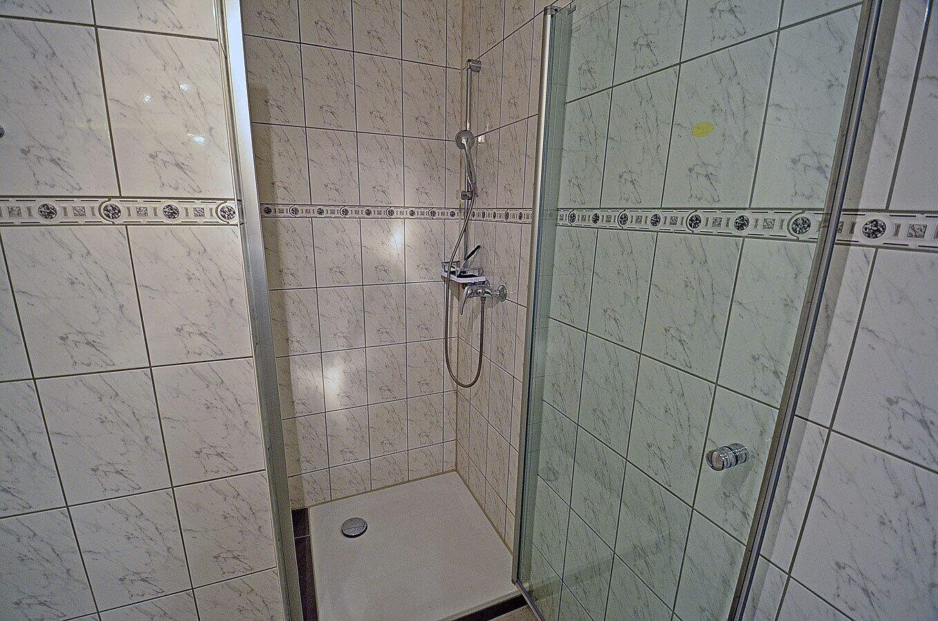 Ein Badezimmer mit einer Duschkabine aus Glas, einem marmorverkleideten Duschbereich und einem kleinen Waschbecken.
