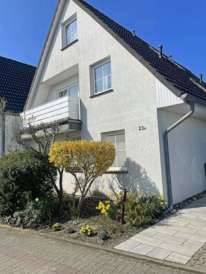 A two-story building with a white exterior, a visible number '23', and a small garden with yellow flowers. - On the 1st floor of the Breege residential complex, quiet location, dog-friendly, about 900 meters from the beach (Breege)