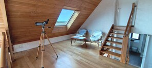 A room with a wooden ceiling, a telescope on a tripod, two striped chairs, and a wooden ladder.