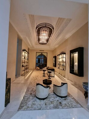 A hallway with a patterned carpet, a central seating area with two chairs and a table, and shelves with items on either side.