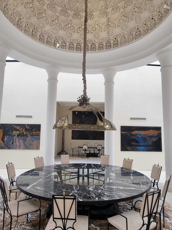 A circular marble table with chairs, a chandelier, and artwork on the walls.
