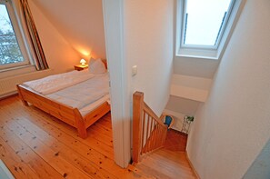 Ein Schlafzimmer mit einem hölzernen Bett, einem Nachttisch mit Lampe, einem Fenster und einer Treppe zu einer oberen Ebene.