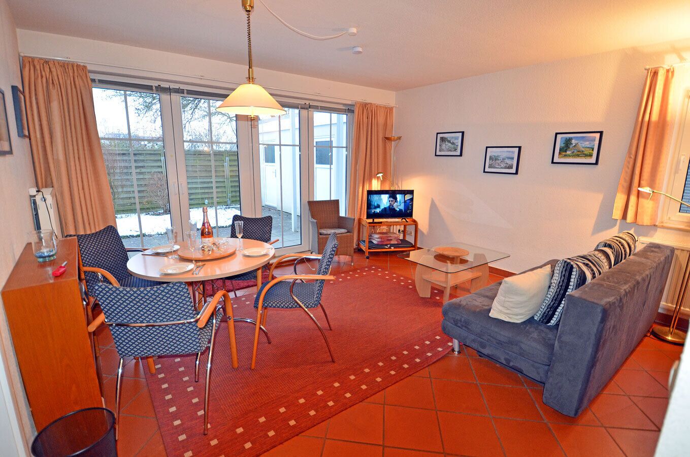 A living room with a sofa, a dining table with chairs, a television, and a window with curtains.