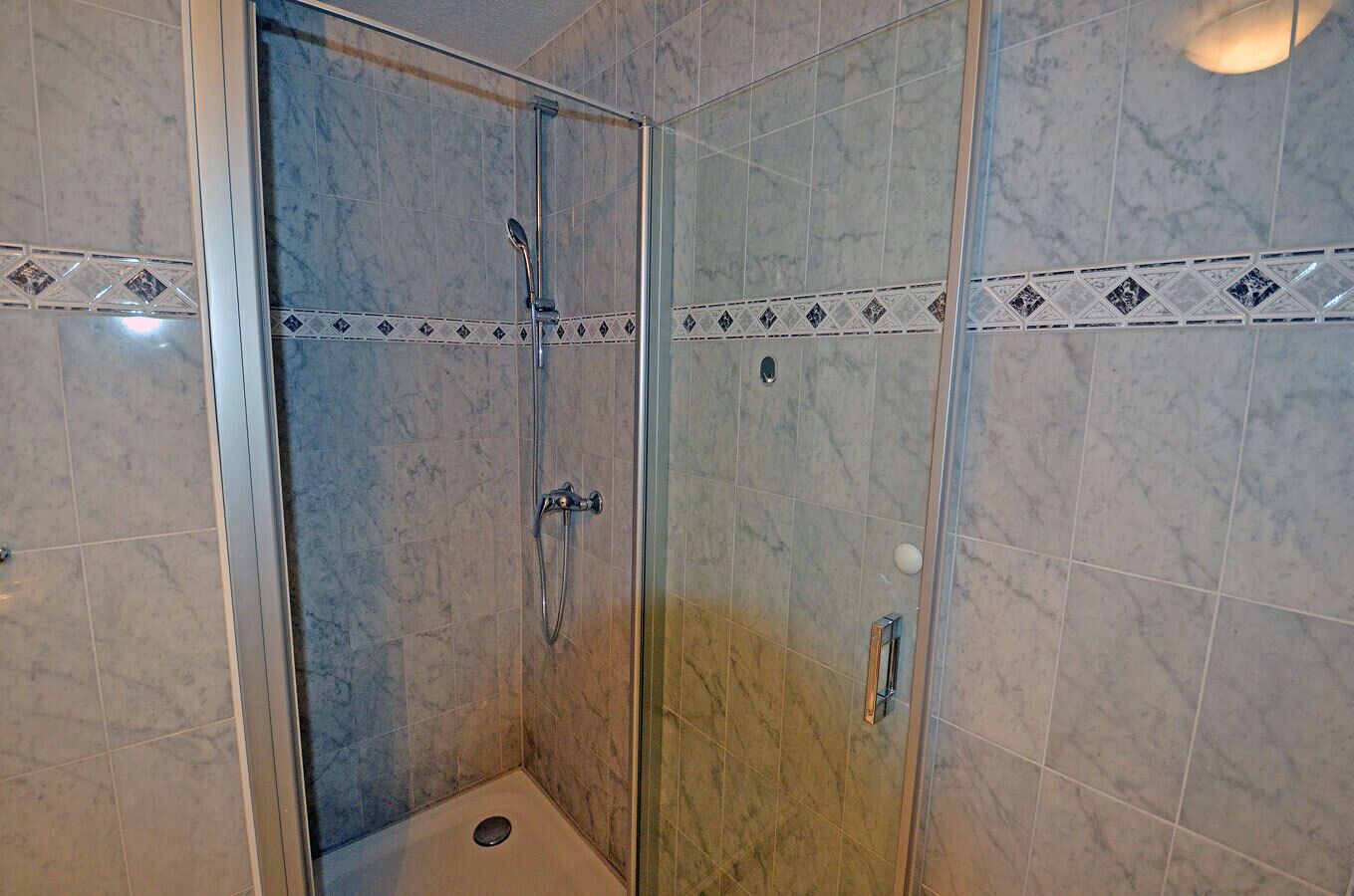 A glass-enclosed shower with a handheld showerhead and a wall-mounted faucet.