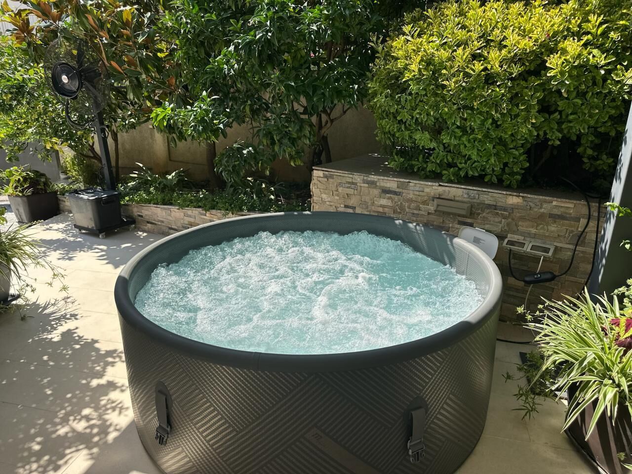 A hot tub outdoors with a stone wall and greenery in the background.