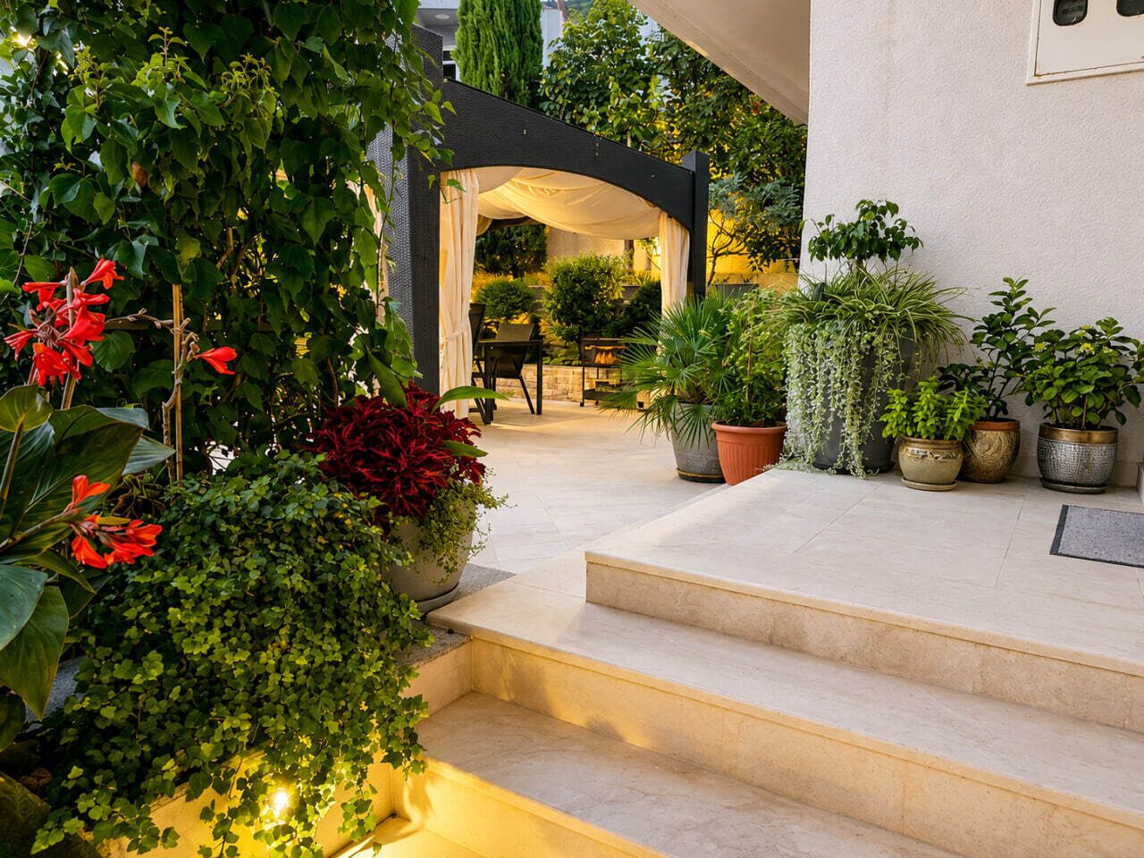 A well-maintained outdoor area with steps leading to a covered seating area, surrounded by various potted plants and greenery.