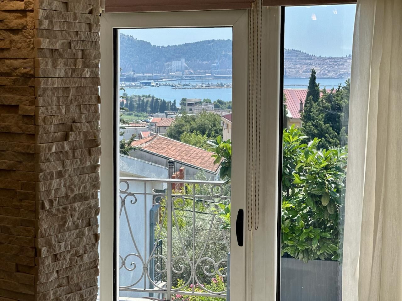 A view from a balcony with a metal railing, overlooking a body of water, buildings, and greenery.