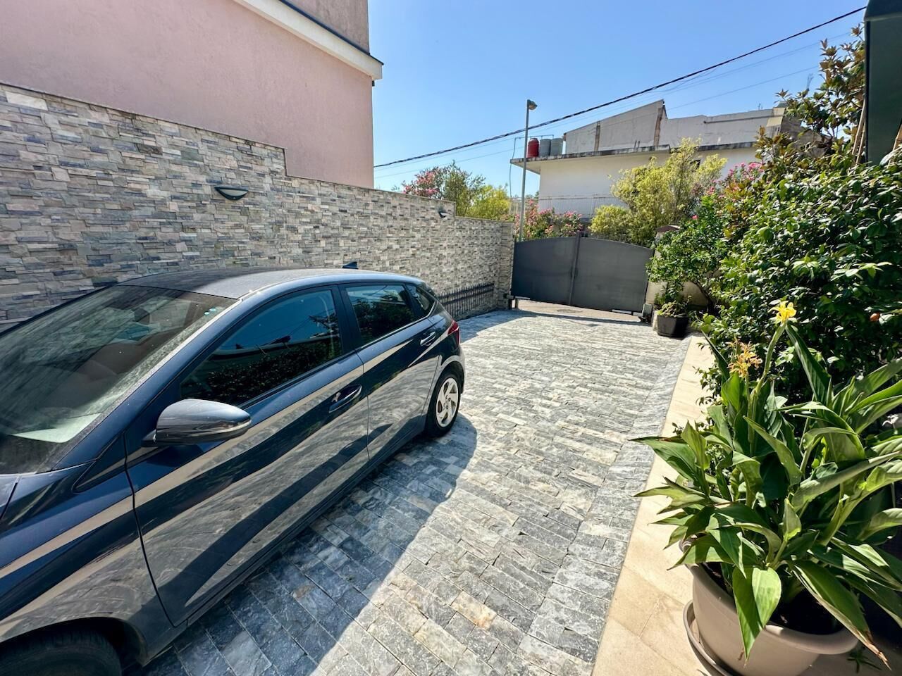 A car parked in a driveway with a stone wall and potted plants.