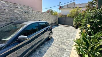 A car parked in a driveway with a stone wall and potted plants.