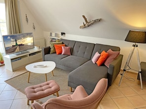 Ein modernes Wohnzimmer mit einem grauen Ecksofa, einem weißen Couchtisch und einem rosafarbenen Sessel.