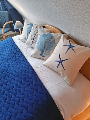 Ein Bett mit blauer Steppdecke und Kissen mit Meereskreaturen-Motiven.