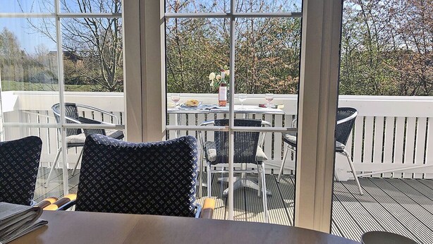 A sunlit outdoor dining area with a table, chairs, and a view of a garden through large windows. - Only 900 meters from the beach, 1st floor with balcony, Internet/Wi-Fi, washing machine (Breege)