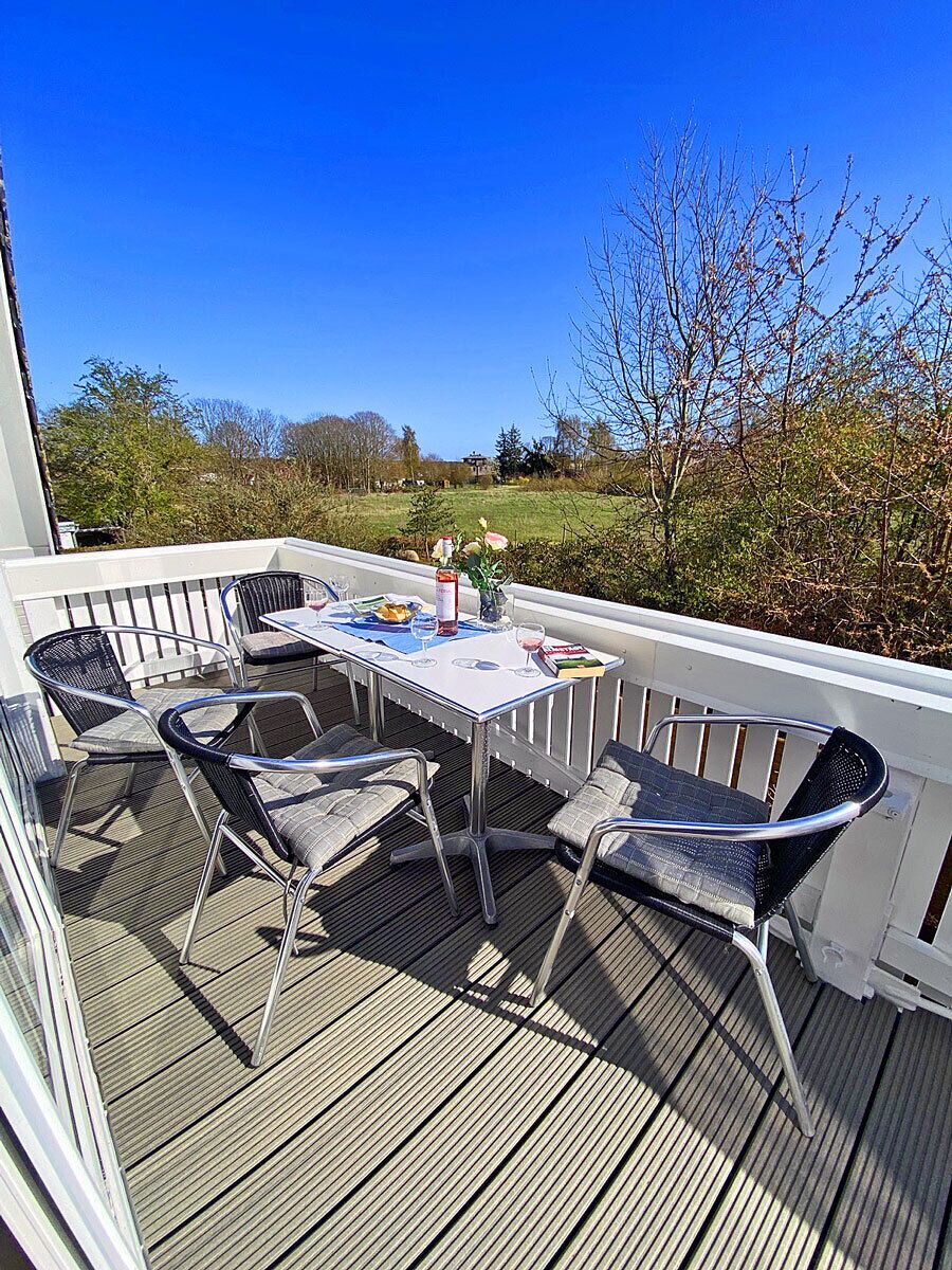Une terrasse extérieure avec une table et des chaises, une vue sur le paysage et une rambarde blanche.