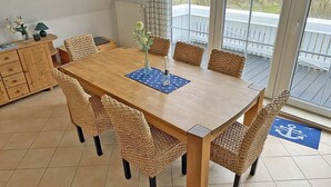 A dining area with a wooden table and woven chairs, a vase with flowers, and a view of a deck through large windows. - Only 900 meters from the beach, 1st floor with balcony, Internet/Wi-Fi, washing machine (Breege)
