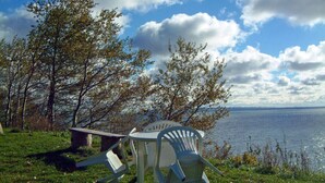 Una mesa de picnic y sillas junto a un lago, con árboles al fondo.
