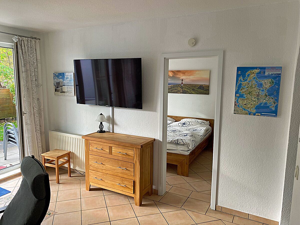 A bedroom with a bed, a wooden dresser, a television, and a window with curtains.