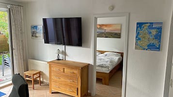 A bedroom with a bed, a wooden dresser, a television, and a window with curtains.