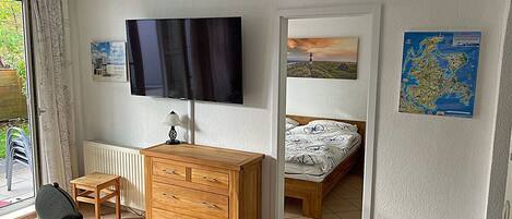 Een slaapkamer met een bed, een houten dressoir, een televisie en een raam met gordijnen.