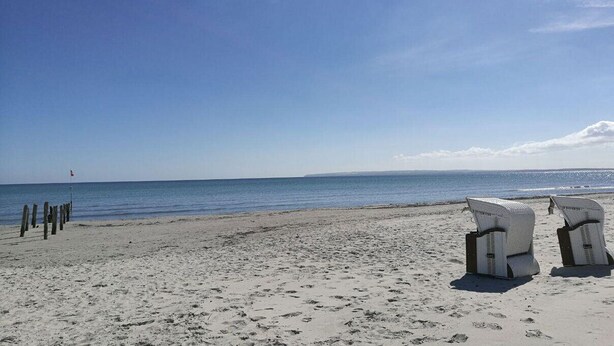 Une plage avec un ciel dégagé, un rivage sablonneux et deux chaises en osier tournées vers la mer.